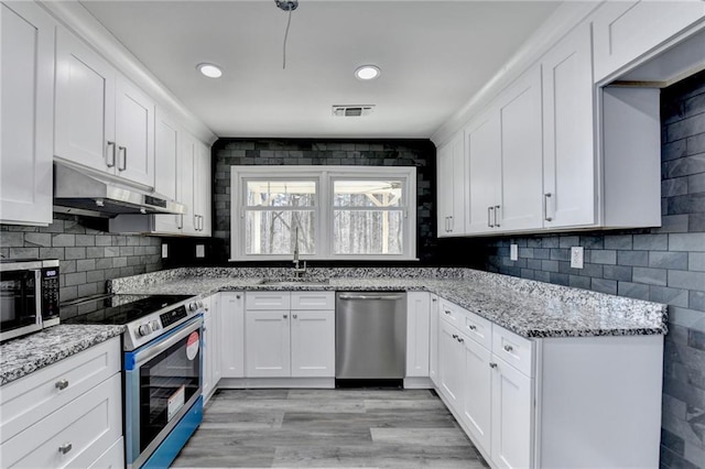 kitchen with under cabinet range hood, decorative backsplash, stainless steel appliances, white cabinetry, and a sink