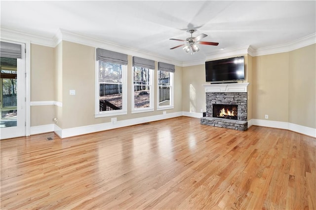 unfurnished living room with light wood-style flooring, a fireplace, a ceiling fan, baseboards, and crown molding