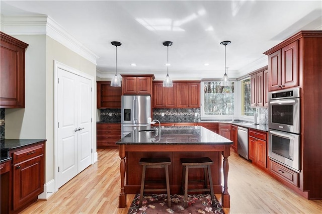 kitchen with reddish brown cabinets, hanging light fixtures, appliances with stainless steel finishes, and an island with sink