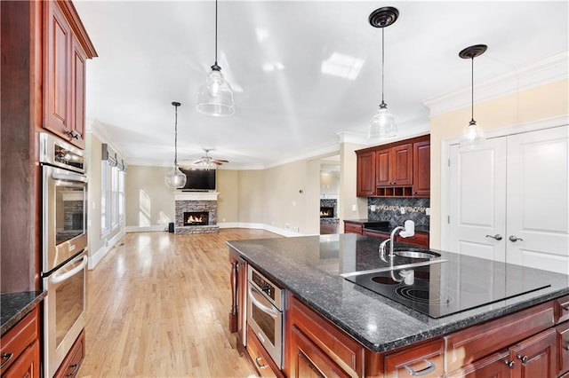 kitchen featuring black electric stovetop, a stone fireplace, stainless steel double oven, open floor plan, and a center island with sink