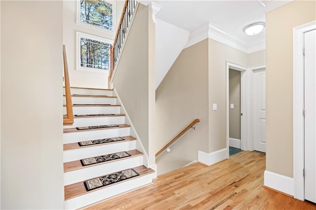 stairway featuring baseboards, wood finished floors, and crown molding