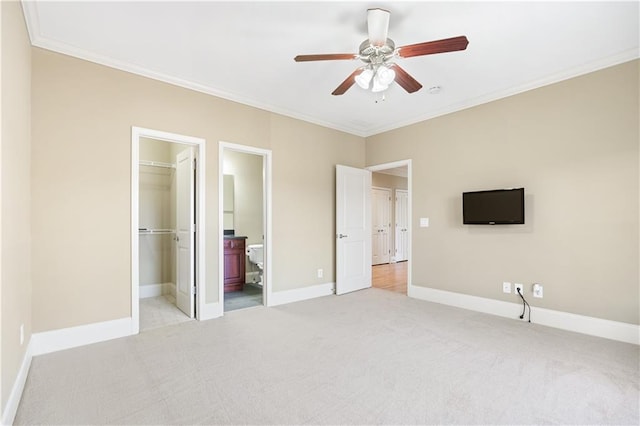 unfurnished bedroom featuring ornamental molding, a walk in closet, light carpet, and baseboards