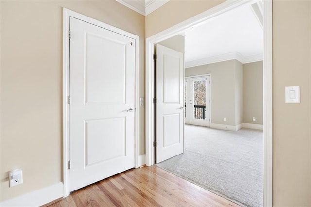 hallway with light wood-type flooring, baseboards, crown molding, and light colored carpet