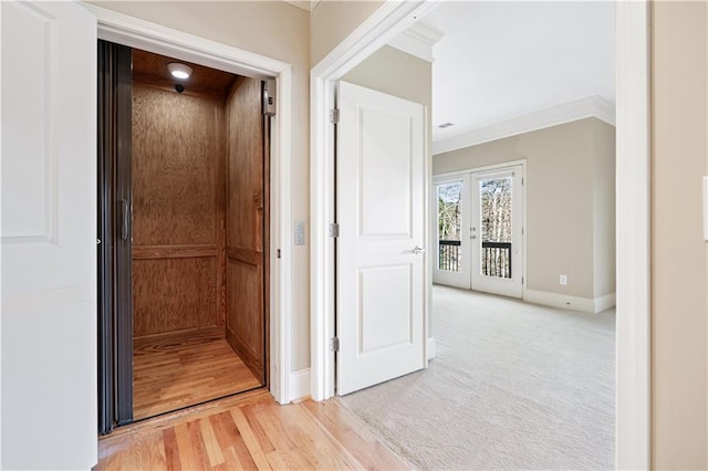 hallway featuring light colored carpet, baseboards, ornamental molding, french doors, and elevator