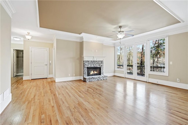 unfurnished living room with ceiling fan, a stone fireplace, baseboards, light wood finished floors, and crown molding