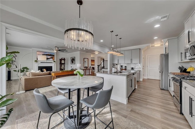 kitchen with tasteful backsplash, a center island with sink, appliances with stainless steel finishes, a lit fireplace, and crown molding