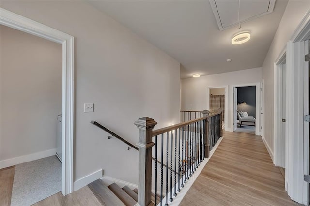 hall featuring attic access, light wood-type flooring, baseboards, and an upstairs landing