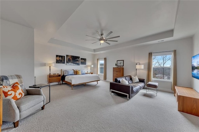 bedroom with a ceiling fan, a tray ceiling, and light colored carpet