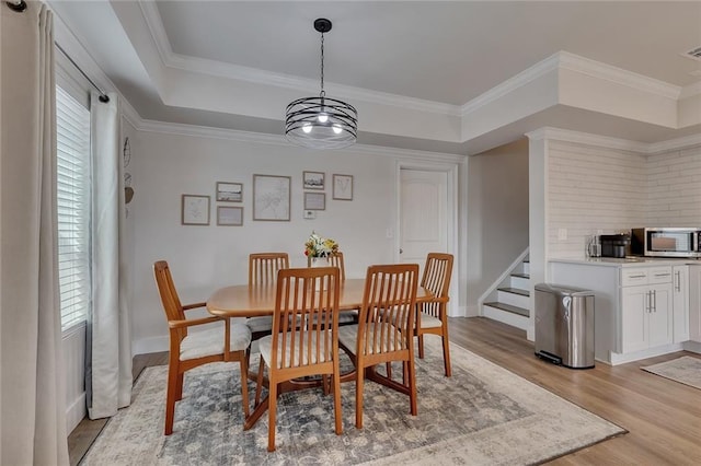 dining space featuring a raised ceiling, crown molding, light wood-style flooring, and stairs