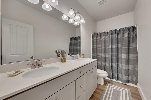 bathroom featuring toilet, wood finished floors, a sink, and visible vents