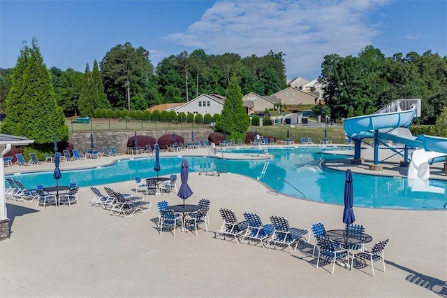 pool featuring a water slide, fence, and a patio