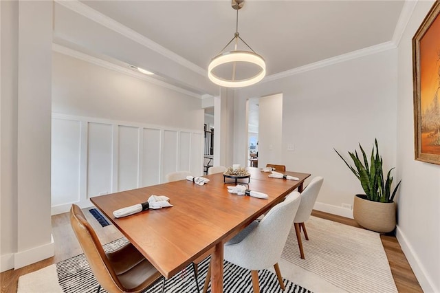 dining area with a wainscoted wall, a decorative wall, light wood-style flooring, and crown molding