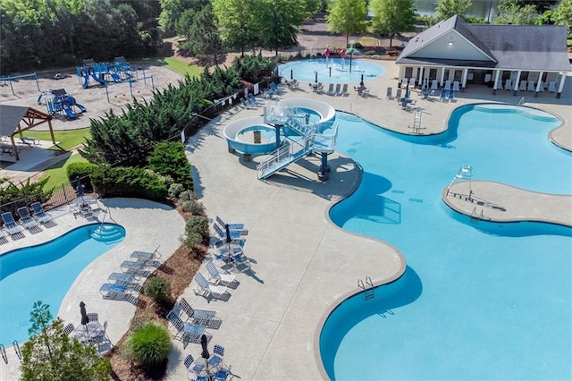 community pool with a water slide, a patio area, fence, and a water play area