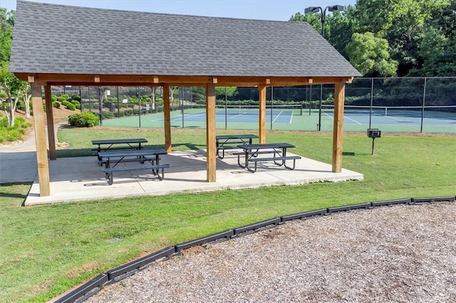 view of home's community featuring a tennis court, fence, and a lawn