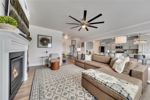 living room featuring ceiling fan, light wood-style floors, baseboards, a glass covered fireplace, and crown molding