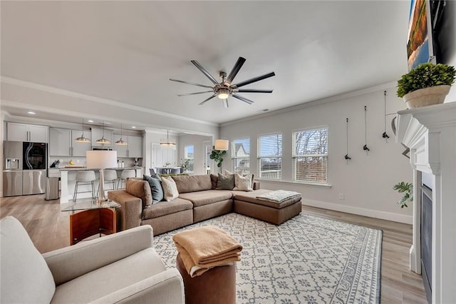 living area with baseboards, light wood-style flooring, ceiling fan, ornamental molding, and a fireplace