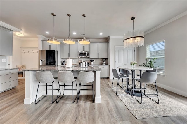 kitchen featuring light stone counters, stainless steel microwave, fridge with ice dispenser, an island with sink, and a kitchen bar