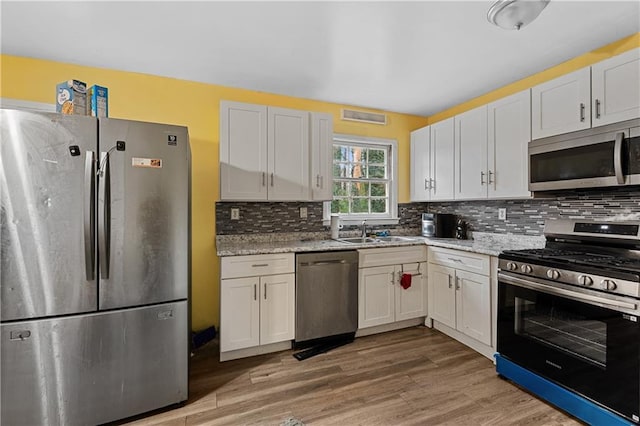 kitchen featuring light stone counters, backsplash, white cabinetry, and appliances with stainless steel finishes