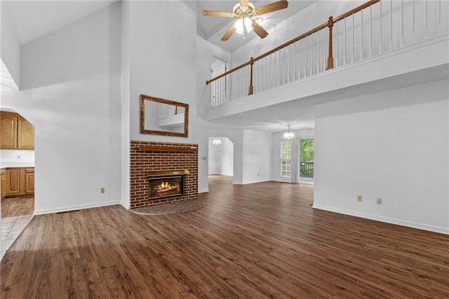 unfurnished living room featuring a towering ceiling, dark hardwood / wood-style flooring, a fireplace, and ceiling fan