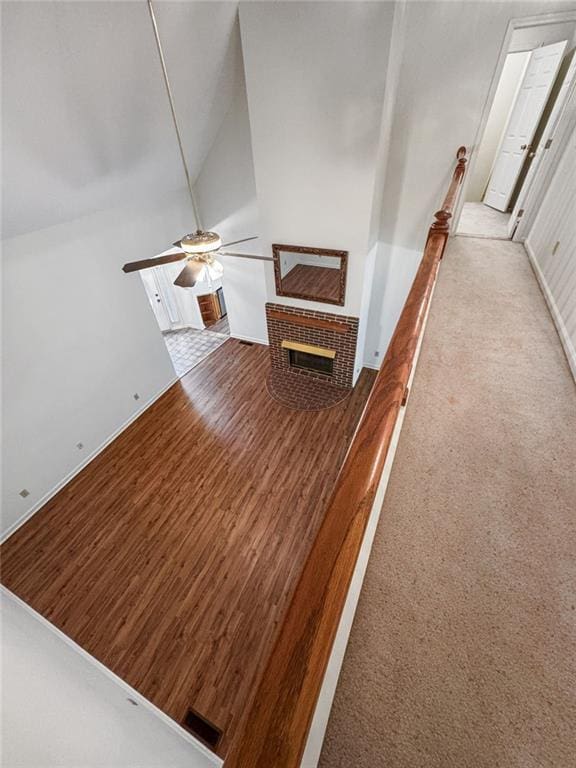 staircase featuring lofted ceiling, a brick fireplace, and ceiling fan