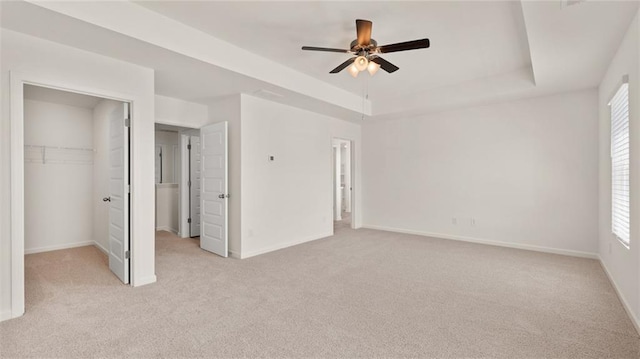 unfurnished bedroom featuring light colored carpet, a tray ceiling, and a spacious closet