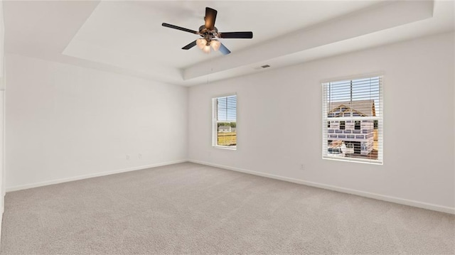 empty room with a tray ceiling, light carpet, baseboards, and ceiling fan