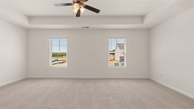 carpeted spare room with a raised ceiling, ceiling fan, and baseboards