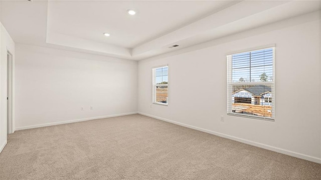 spare room featuring light carpet, baseboards, recessed lighting, and a raised ceiling