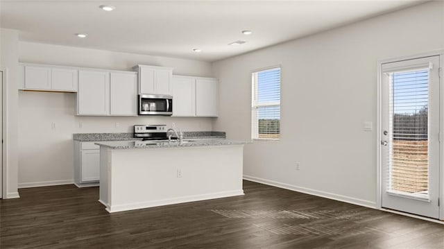 kitchen featuring stainless steel microwave, baseboards, a kitchen island with sink, white cabinets, and recessed lighting