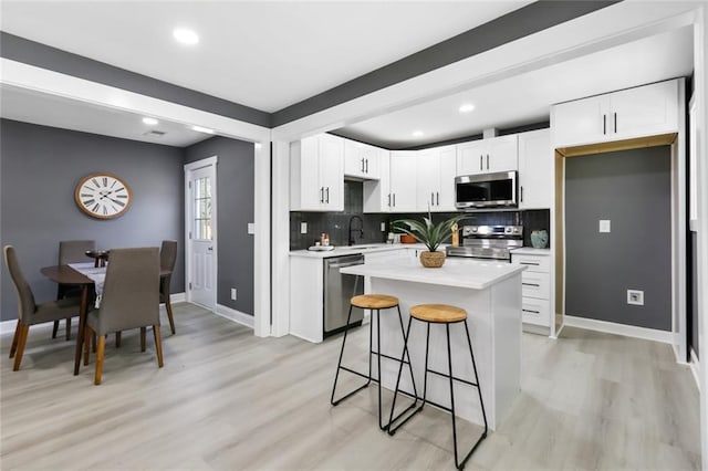 kitchen with a kitchen island, white cabinetry, appliances with stainless steel finishes, a kitchen breakfast bar, and sink