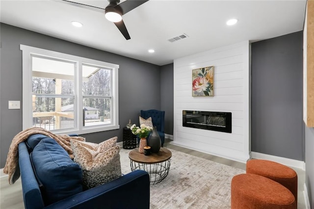 living room featuring a fireplace, ceiling fan, and light hardwood / wood-style floors