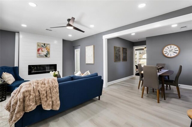 living room featuring a fireplace, light wood-type flooring, and ceiling fan