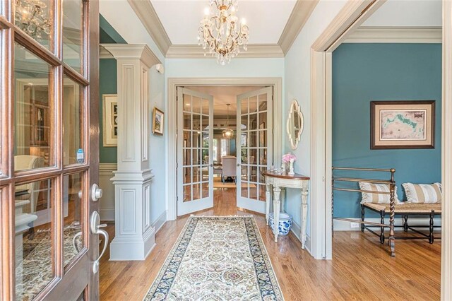 foyer entrance with crown molding, french doors, light hardwood / wood-style floors, a notable chandelier, and decorative columns