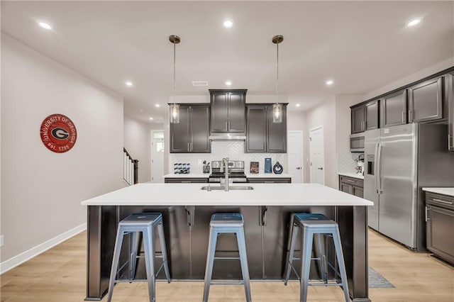 kitchen with a breakfast bar, stainless steel appliances, a kitchen island with sink, sink, and decorative light fixtures