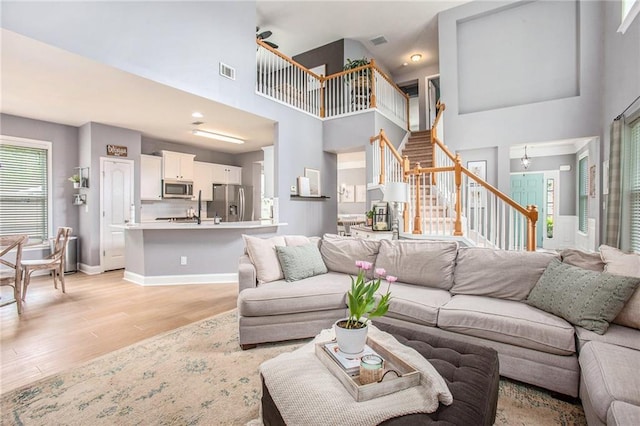 living room featuring a towering ceiling, stairs, light wood-style flooring, and visible vents