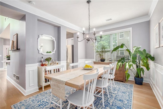 dining area with an inviting chandelier, wainscoting, visible vents, and light wood-type flooring