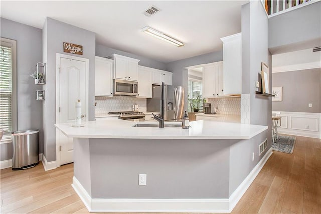 kitchen featuring white cabinets, a sink, light wood-style flooring, stainless steel appliances, and tasteful backsplash