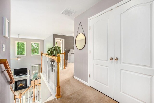 hall featuring carpet floors, baseboards, visible vents, and an upstairs landing