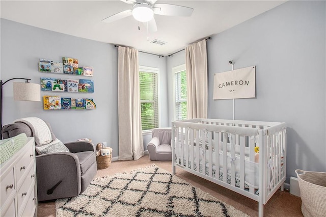 bedroom with visible vents, carpet floors, baseboards, a crib, and a ceiling fan
