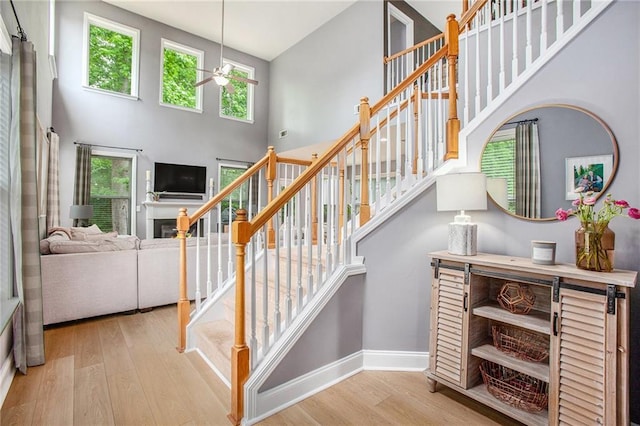stairway with ceiling fan, a towering ceiling, a fireplace, wood finished floors, and baseboards