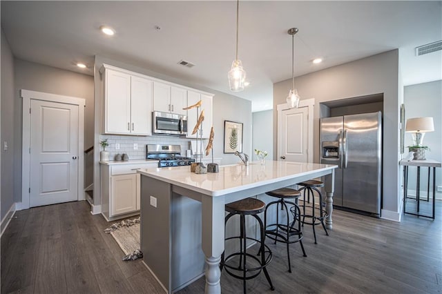 kitchen featuring hanging light fixtures, stainless steel appliances, a kitchen island with sink, dark hardwood / wood-style floors, and backsplash