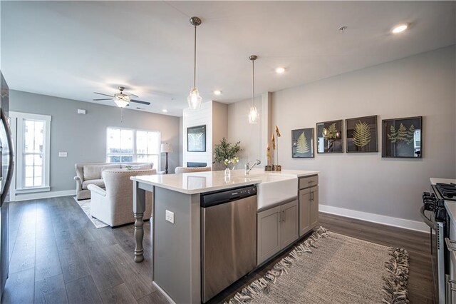 kitchen featuring ceiling fan, stainless steel appliances, a center island with sink, dark hardwood / wood-style flooring, and hanging light fixtures