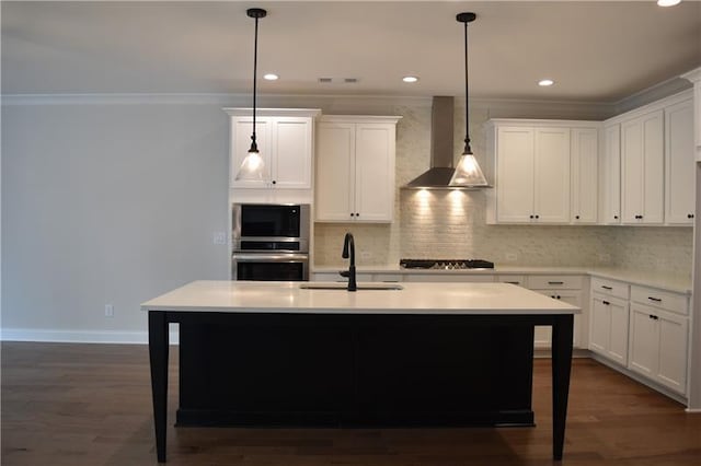 kitchen with a kitchen island with sink, wall chimney range hood, hanging light fixtures, sink, and stainless steel appliances