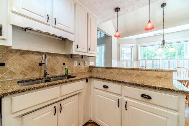 kitchen with a peninsula, tasteful backsplash, pendant lighting, and a sink