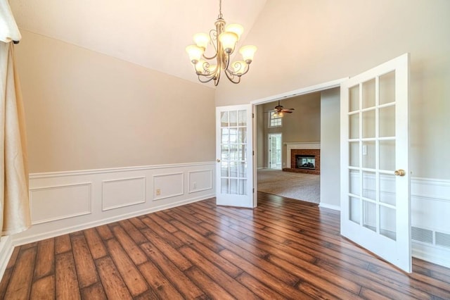unfurnished room with french doors, ceiling fan with notable chandelier, wood finished floors, a fireplace, and a high ceiling