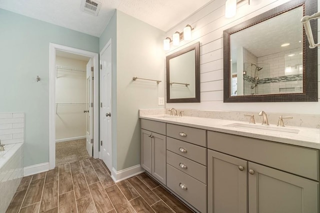 full bath featuring double vanity, a tile shower, a sink, wood tiled floor, and visible vents
