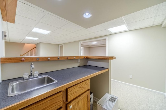 kitchen with baseboards, carpet flooring, a sink, a paneled ceiling, and dark countertops