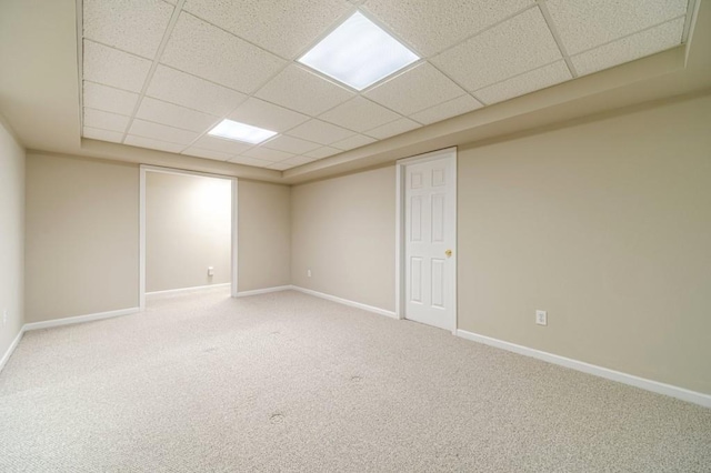 carpeted empty room with a drop ceiling and baseboards