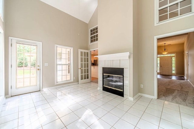 unfurnished living room with baseboards, a tiled fireplace, high vaulted ceiling, and light tile patterned flooring