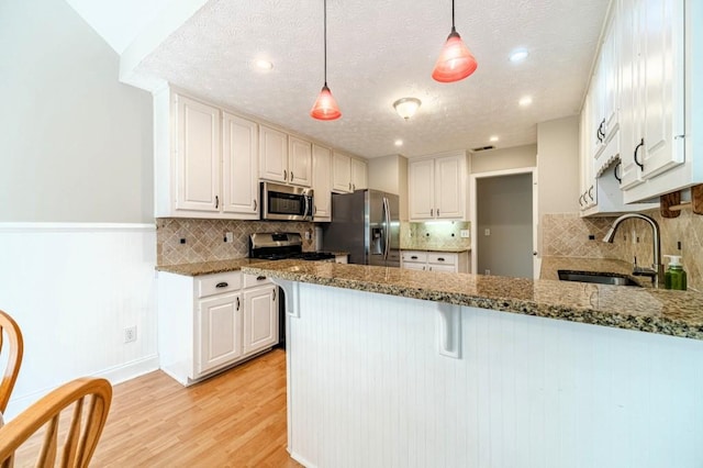 kitchen with a sink, a peninsula, light wood-type flooring, stone counters, and appliances with stainless steel finishes